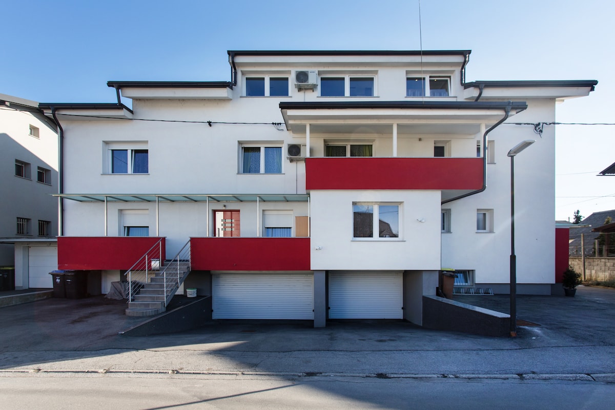 Bijelo-crveno ožbukano pročelje kuće Patricia House, trokatnice s balkonima, garažama s roletama u prizemlju i parkiralištem ispred