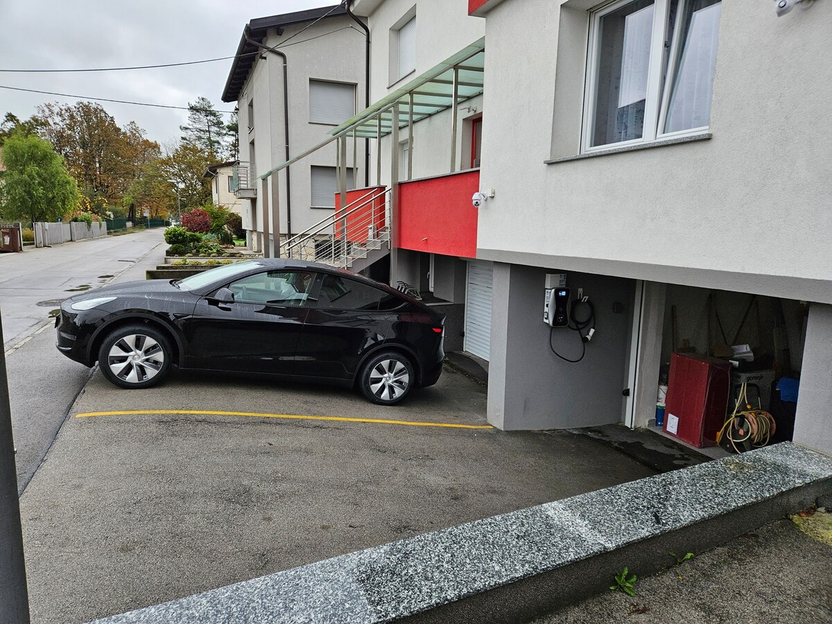 Automobil parkiran na označenom mjestu uz kuću, s punionicom za električna vozila postavljenom na zid pokraj otvorene garaže