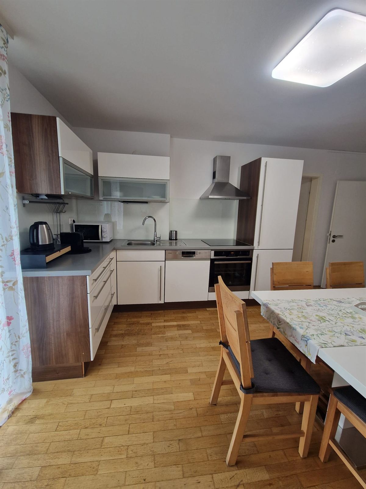 Angolo cucina con mobili bianchi e pensili in legno scuro, una cappa sopra il piano cottura, un forno sotto, e un bollitore e un tostapane sul piano di lavoro